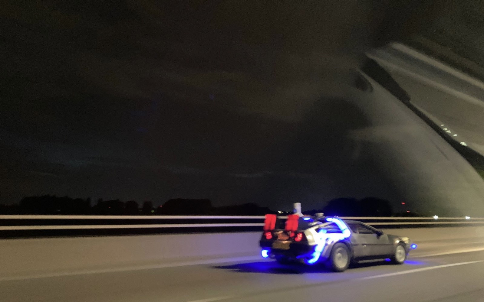 DeLorean driving at night with blue neon lights glowing